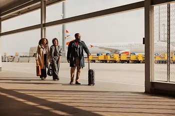 People with carry-on luggage in the outdoor area of Vienna International Airport on their way to the terminal.
