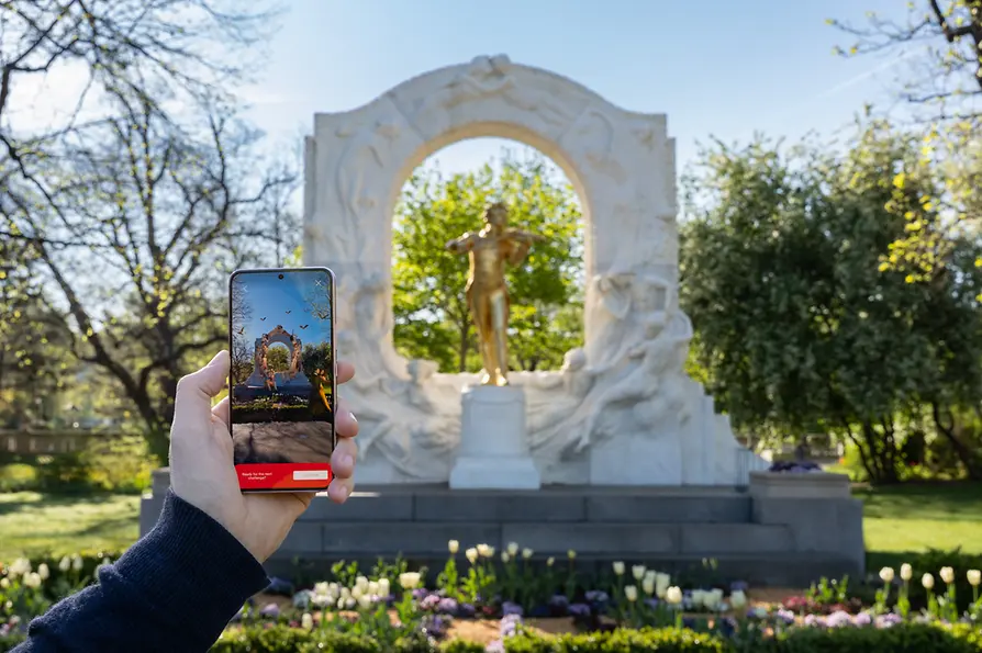 Johann Strauss monument in the city park with smartphone in the foreground